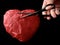 Red heart with scissors, on a black background. Paper heart with a slot inside. Crumpled paper in the shape of a heart. Concept: