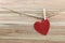 Red heart shape hanging on a hemp rope on brown wood background.