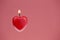 Red heart shaped candle burning, pink textured background