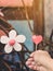 A red heart-shaped candle on woman`s hand and an artificial flower made of white and red candles with bluerd image of rusty steel