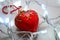 Red heart-shaped christmas ornament surrounded by chrismas lights on neutral marble surface.