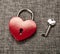 Red heart shaped padlock with a key on gray linen