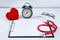 Red heart and stethoscope, alarm clock with clipboard on table