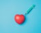 Red heart and stuck needle of a plastic syringe inside of it on a blue background