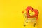 Red heart in the supermarket trolley. concept of buying love. Valentine`s Day. yellow background. Love of shopping. Favorite stor