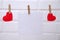 Red hearts are hung on the rope with clothespins with a sheet of paper on a white background.