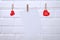 Red hearts are hung on the rope with clothespins with a sheet of paper on a white background.