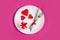 Red hearts on a white plate  a fork  a knife  a gift box on a pink background  top view  copy space. Valentine`s day