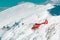 A red helicopter flying in snow cowered mountains