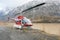 A red helicopter sits idly by a mountain lake