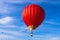 Red hot air balloon against blue cloudy sky