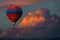 Red hot air balloon floating in beautiful colorful storm clouds at sunset