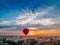 Red hot air balloon flying over small european city at summer sunrise