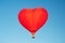 Red hot air balloon in the shape of a heart in clear blue sky. Aerostat over the field landscape