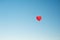 Red hot air balloon in the shape of a heart in clear blue sky. Aerostat over the field landscape.