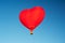 Red hot air balloon in the shape of a heart in clear blue sky. Aerostat over the field landscape. Close up