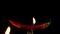 Red hot chili pepper on fork in flames on black background