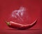 Red hot chili pepper on red background with smoke. Still life with steam mexican paprika