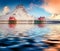 Red houses and huge snowy peaks reflected in calm waters of Hovdanvika Flord.