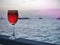 Red iced cold beverage in wine glass on wood piece with sunset background of open sea and silhouette boats