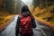 In a red jacket and with a backpack, a woman walks forested roads