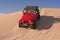 Red Jeep driving down a sand dune