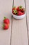 Red juicy strawberries in white bowl on wooden background with stripes