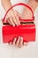 Red lacquered bag in female hands.