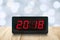 Red led light illuminated numbers 2018 on digital electric alarm clock face on wooden table top with pastel Christmas lights bokeh