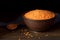 Red lentils in clay bowl with spoon and fabric on rustic wooden table.