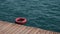 Red lifebuoy or safety ring floating near the dock in blue sea water. Life saving equipment in use. Be careful while swimming in