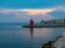 Red lighthouse on coastline of Adriatic sea with colorful houses at sunset, Piran, Slovenia