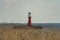 Red lighthouse in the ocean with reed in the foreground