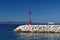 Red lighthouse in port with stones and white bench. Podgora, Croatia