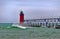 Red lighthouse on a windy day with waves and spray