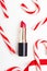 Red lipstick and candy canes top view composition. Beauty industry product concept. Makeup accessory and lollipops on white. Women