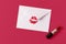 Red lipstick kiss on white envelope on magenta background.