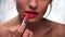 Red Lipstick. Woman applying lipstick on full lip closeup