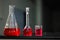 Red liquid in a round bottomed flask and glass beaker and conical flask on a black granite table in dark background