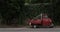 Red, little retro car on the road among green wall of plants. Typical red and green italian picture. in dark, dull colors.