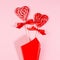 Red lollipops hearts with silk bow as festive bouquet on pastel pink as  romantic love background, square.