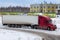 Red long-distance bonnet truck with a white semitrailer in the countryside