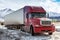 Red long-distance bonnet truck with a white semitrailer at winter on the background of high picturesque mountains