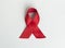 Red medical ribbon for AIDS and HIV day awareness. Curled satin bow on blue background