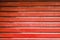 Red metal automatic garage shutter closeup, steel striped sliding door,  texture and pattern, old and weathered surface, dirty
