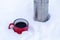 Red metal cup with coffee poured from a thermos on pure white snow in the forest while walking