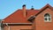 A red metal roofing construction of a red brick house with roof gutters, downpipe, soffit, fascia and box end, an attic window,