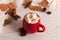 Red mug with cocoa and marshmallows, on a background of a scarf and dry leaves. Autumn mood, a warming drink