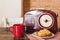 A red mug with coffee, a radio in retro style and pastries are on the wooden table