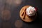 Red mug with hot chocolate or cocoa with whipped cream on a wooden stand with cinnamon sticks on a dark background with a garland